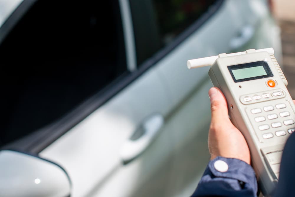 Police officer holding a portable breathalyzer device near a white car during a DUI traffic stop.